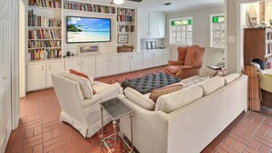 A living room with a sofa, armchairs, a coffee table, a TV, and a bookshelf filled with books. - Poolside Paradise - Historic District Home (College Station)