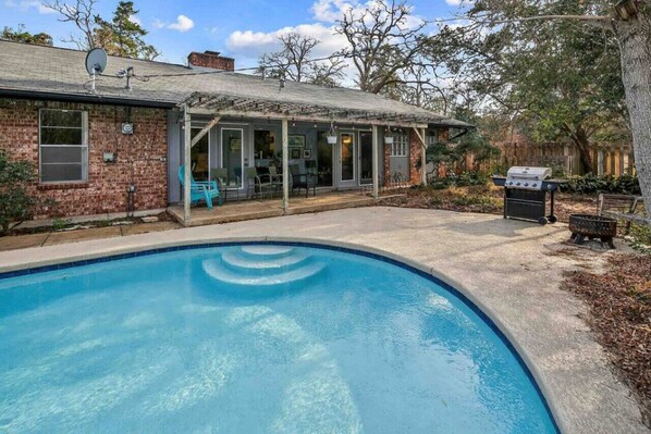 A backyard with a swimming pool, a covered patio, and a barbecue grill.
