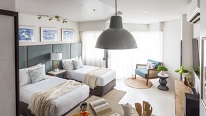 A modern hotel room with two beds, a large pendant light, a small round table, a sofa, and a television. - Cozy Seaside Studio with Balcony Scenic Ocean View (Lapu-Lapy City)