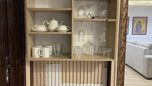 A kitchen area with wooden cabinets, a white countertop, and various kitchenware including teapots, cups, and glassware.