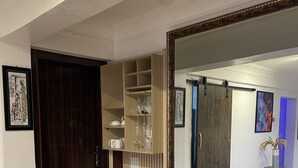 A room with a large mirror, wooden flooring, a dark wooden door, and a white wall with a framed picture.