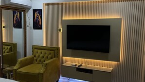 A hotel room with a large bed, a sofa, a TV mounted on a wall, and a ceiling air conditioner.