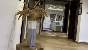 A hallway with a wooden floor, a decorative plant on a wooden stand, and framed artwork on the walls.