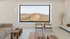 Ein modernes Wohnzimmer mit großem Fenster, einer Couch, zwei Holztischen und zwei Stühlen.
