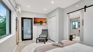 Een moderne slaapkamer met een groot bed, een stoel, een glazen deur en een schilderij van een zonsondergang.