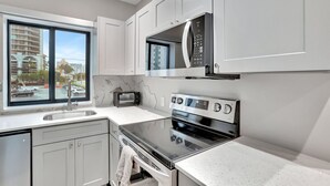 A modern kitchen with white cabinets, a stainless steel microwave, a built-in oven, and a window overlooking a parking area.