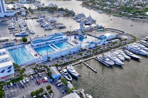Eine Luftaufnahme einer Marina mit zahlreichen dort angestückten Yachten, einem großen Schwimmbad und einem Parkplatz mit Autos.