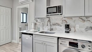 Una cocina moderna con gabinetes blancos, salpicadero de mármol, microondas integrado, cafetera y lavavajillas.