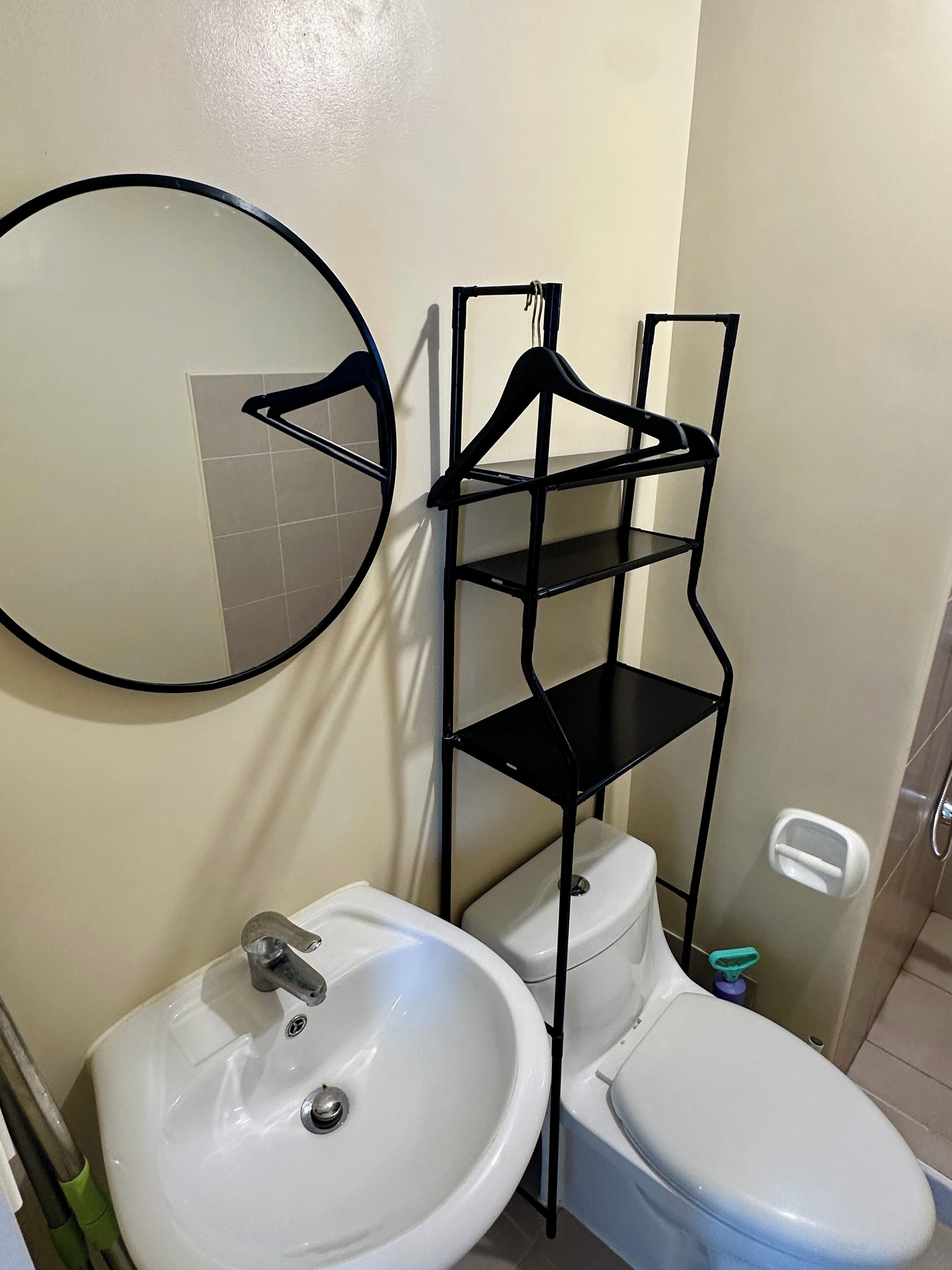 A bathroom with a white sink, toilet, and a black metal shelf unit.