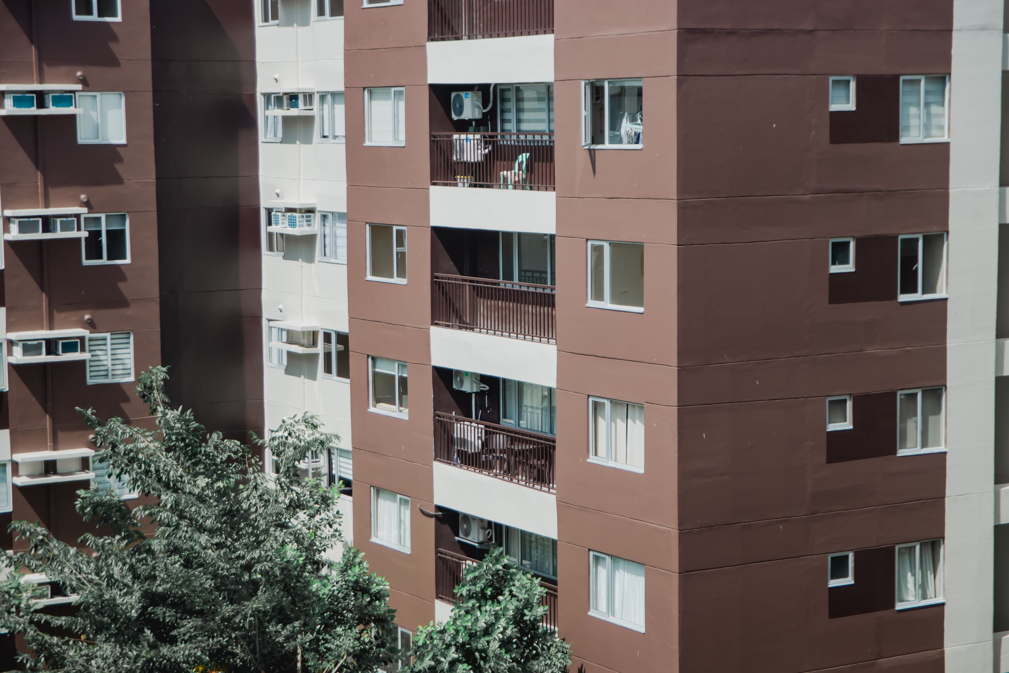 A multi-story residential building with balconies, air conditioning units, and a tree in the foreground.