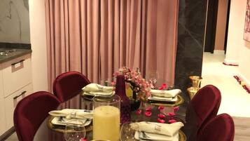 A dining area with a round glass table, red velvet chairs, a gold chandelier, and a backdrop of pink curtains.