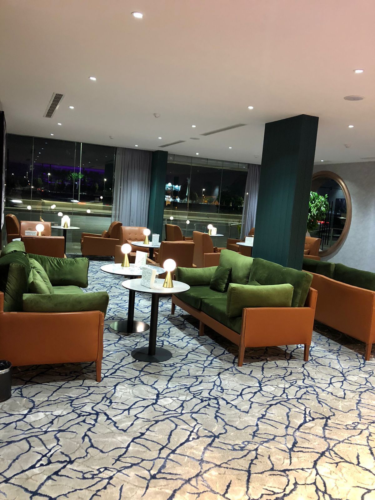 A modern lounge area with green sofas, orange armchairs, and round tables.