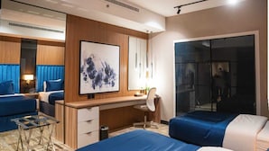 A hotel room with two beds, a desk, a chair, a small table, a mirror, and a painting. - DANA HOTEL RESIDENCES QASSIM (Buraydah)