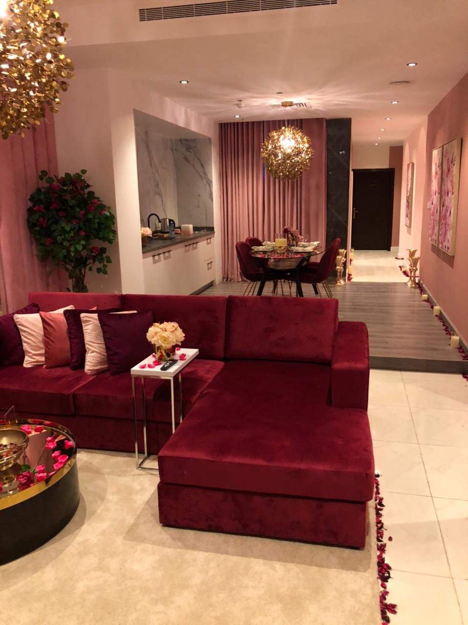 A modern living room with a red sectional sofa, a dining area with a round table, and a large abstract painting on the wall.