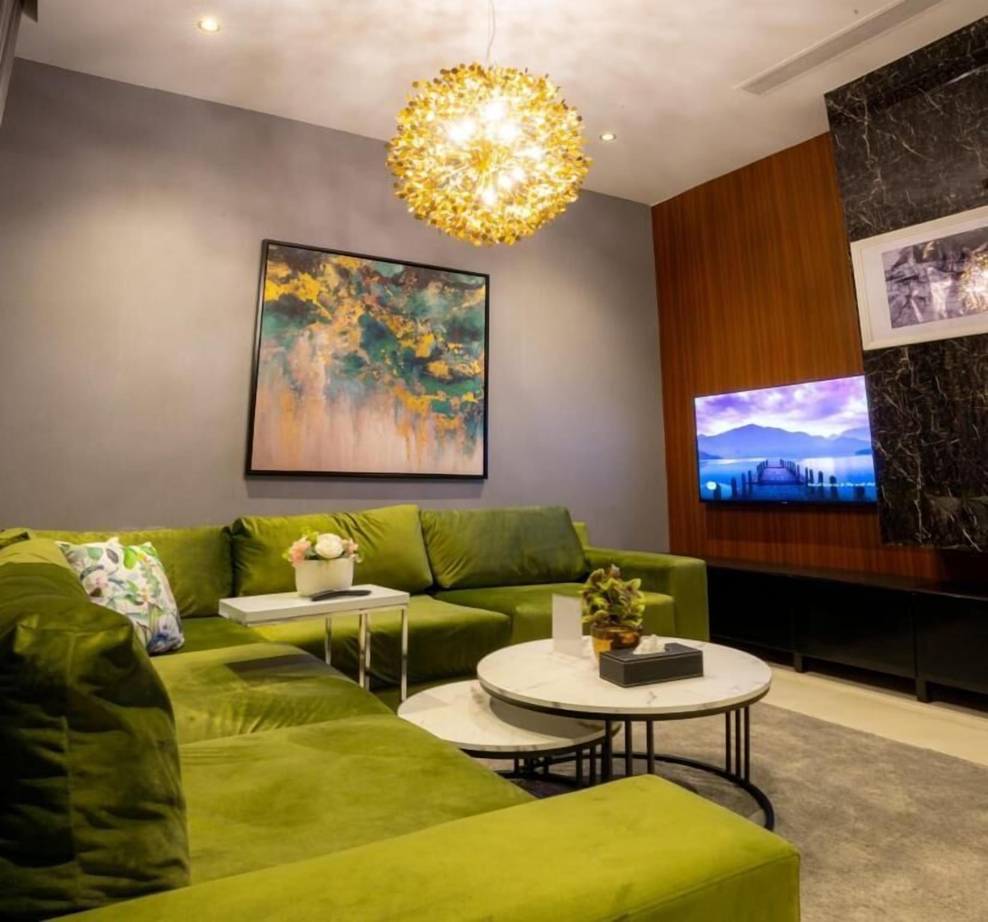 Una sala de estar moderna con un sofá seccional verde, una mesa de centro redonda y un cuadro grande en la pared.