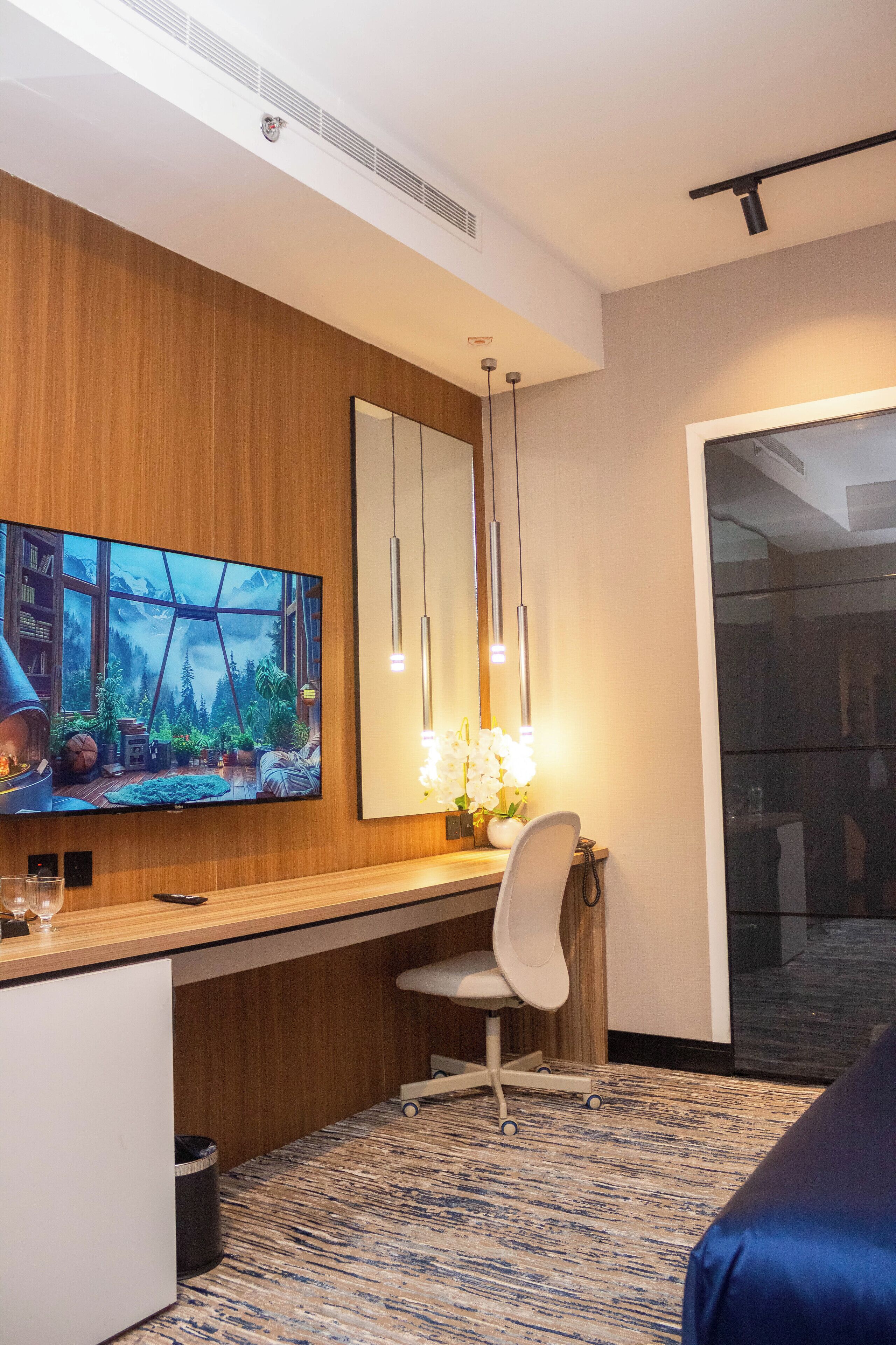 Habitación de hotel moderna con una pared de acento de madera, un televisor de pantalla plana grande, un escritorio con una silla y una puerta de vidrio que da a un balcón.