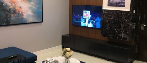 A modern living room with a large TV, blue sofas, a marble coffee table, and a decorative vase.