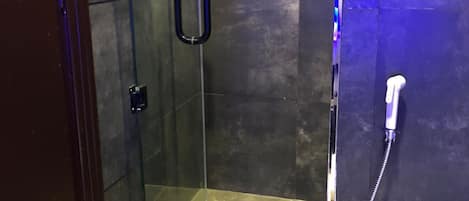 A glass-enclosed shower stall with a handheld showerhead and a wall-mounted faucet.