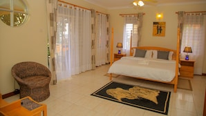 A bedroom with a bed, a chair, a round mirror, and a ceiling fan. - Calm Suites Kampala (Kampala)