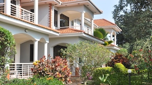 A two-story house with a balcony, surrounded by well-maintained gardens and a variety of plants. - Calm Suites Kampala (Kampala)