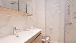 A modern bathroom with a glass-enclosed shower, a white sink with a mirror above, and a toilet with a towel and soap dish.