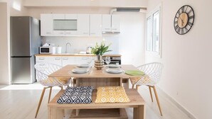 A modern kitchen with white cabinets, a stainless steel refrigerator, and a dining area with a wooden table and two white chairs.
