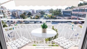 A balcony with white metal railings, two cushioned chairs, a small round table, and a potted plant.
