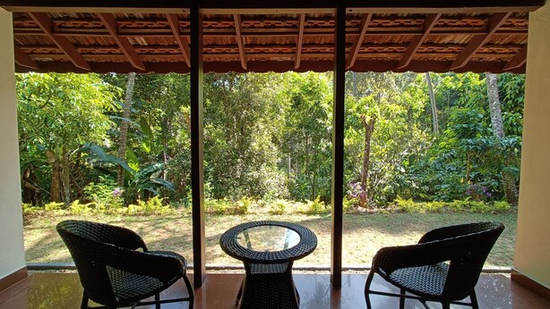Una habitación con una puerta de vidrio que da a un jardín. Hay dos sillas de mimbre y una pequeña mesa redonda.