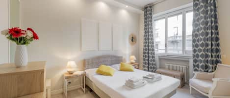 A hotel room with a bed, bedside tables, a chair, a window with curtains, and a view of the outside.