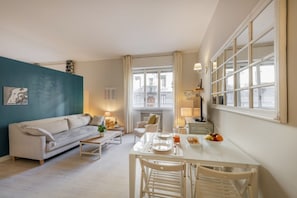 A modern living room with a sofa, dining table, and chairs, a view of the city through large windows, and a teal accent wall.