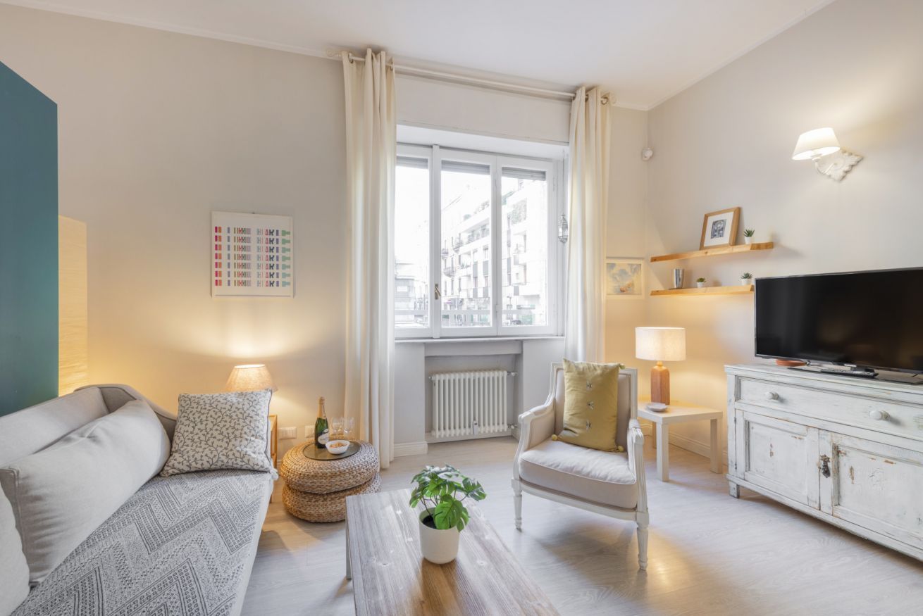 Una sala de estar moderna con un sofá, un sillón, una mesa de centro, televisión y una ventana con cortinas.