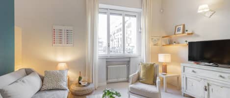 Una sala de estar moderna con un sofá, un sillón, una mesa de centro, televisión y una ventana con cortinas.