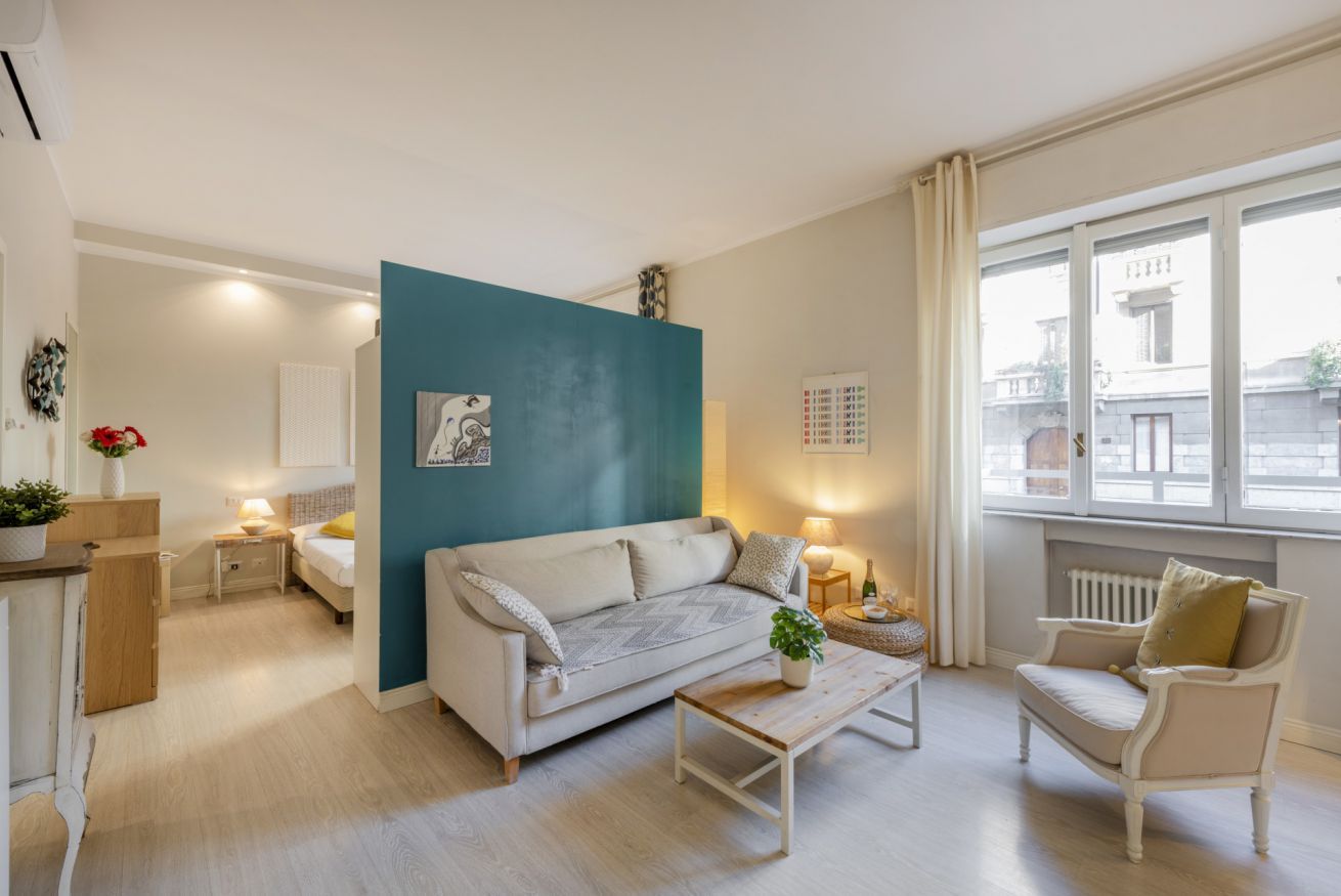 Un salón moderno con sofá, sillón, mesa de centro y vistas de la ciudad a través de amplias ventanas.