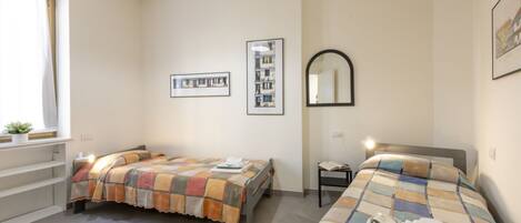 A bedroom with two beds, a window, a bedside table, and a mirror.