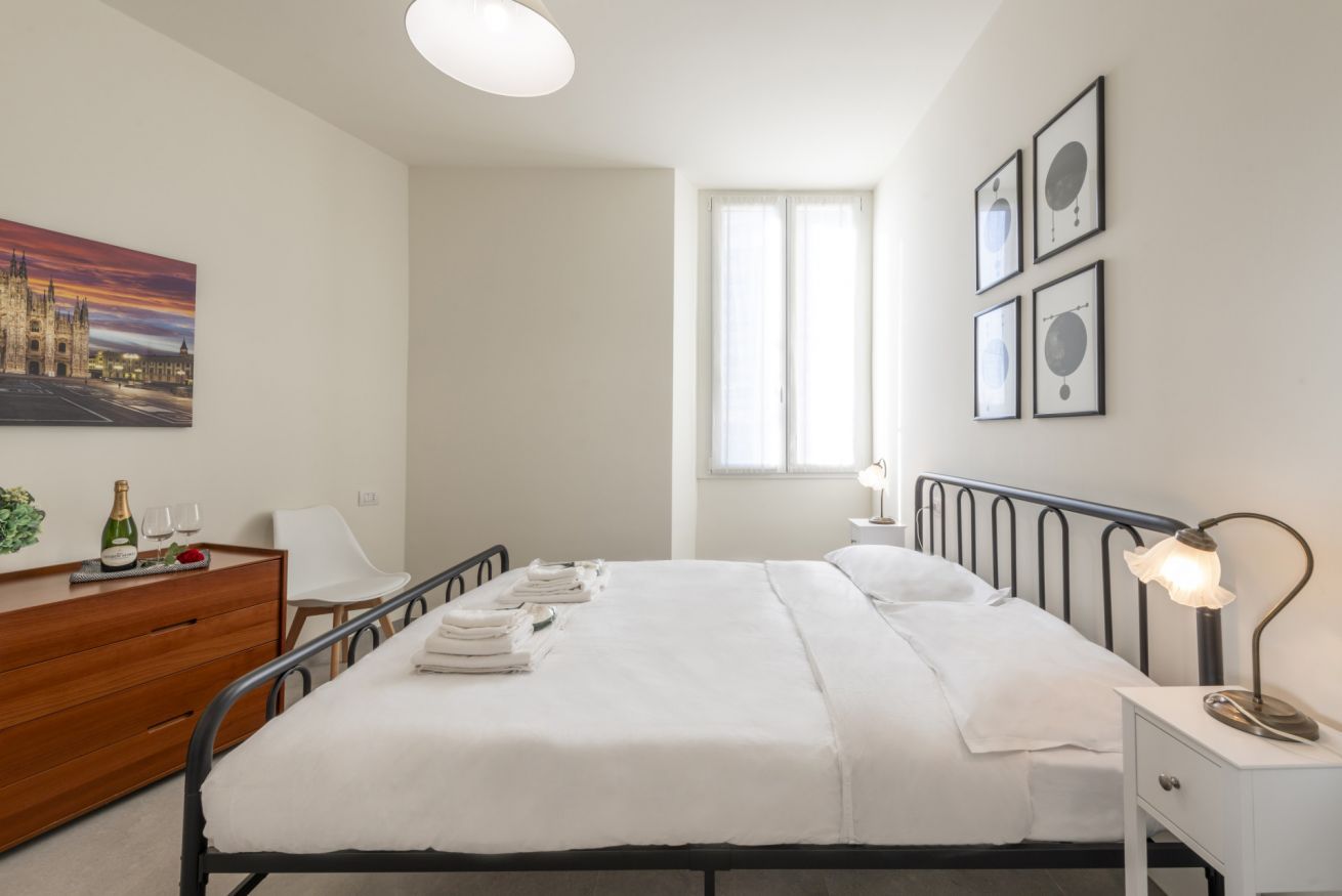 Habitación de hotel con cama, mesita de noche, lámpara y ventana con cortinas.