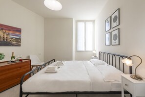 A hotel room with a bed, bedside table, lamp, and a window with curtains.
