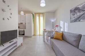 A modern living room with a flat-screen TV, a sofa, a dining area with a table and chairs, and a kitchen in the background. - BnButler - Maloja, 10 (Milano)