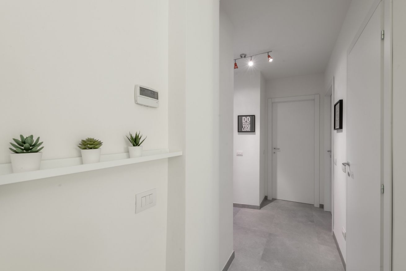 Un couloir aux murs blancs, avec un thermostat et des plantes en pot.