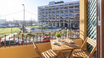 Un balcon avec une table et des chaises, donnant sur un parking et un immeuble à plusieurs étages.