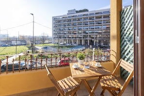 A balcony with a table and chairs, overlooking a parking area and a multi-story building. - BnButler - Maloja, 10 (Milano)