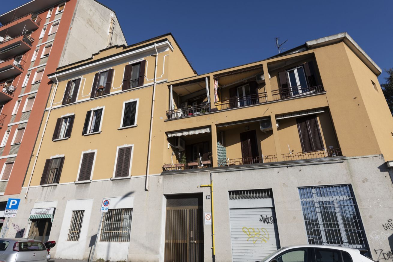 A multi-story building with balconies, a garage door, and a parking sign.