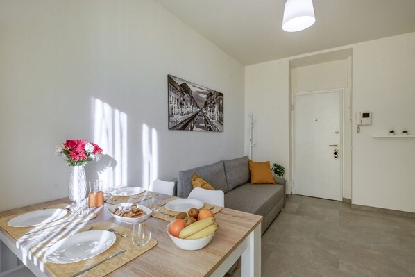 A dining area with a wooden table set for two, a vase with flowers, and a bowl of fruit. - BnButler - Maloja, 10 (Milano)