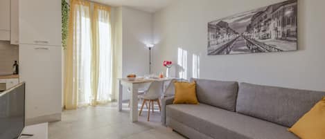 Una sala de estar moderna con un sofá gris, una mesa de comedor y una cocina con armarios blancos.
