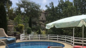 A swimming pool with a wooden deck, white lounge chairs, and a white fence surrounding the area.