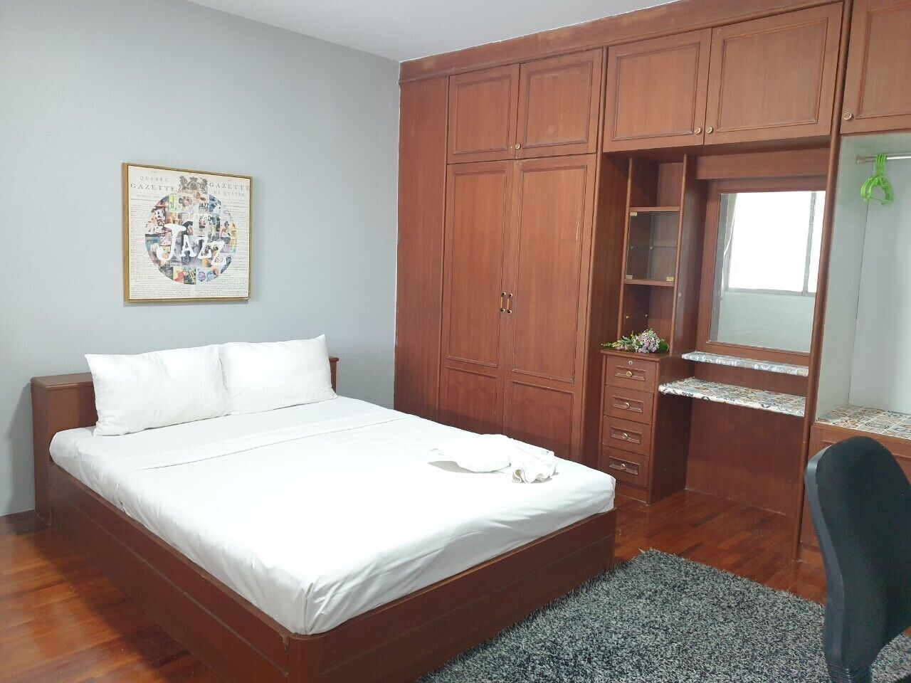 A bedroom with a bed, wooden wardrobe, and a desk with a mirror.