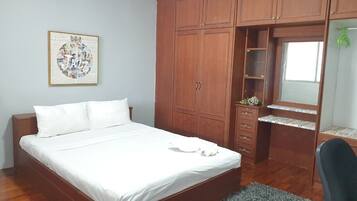 A bedroom with a bed, wooden wardrobe, and a desk with a mirror.