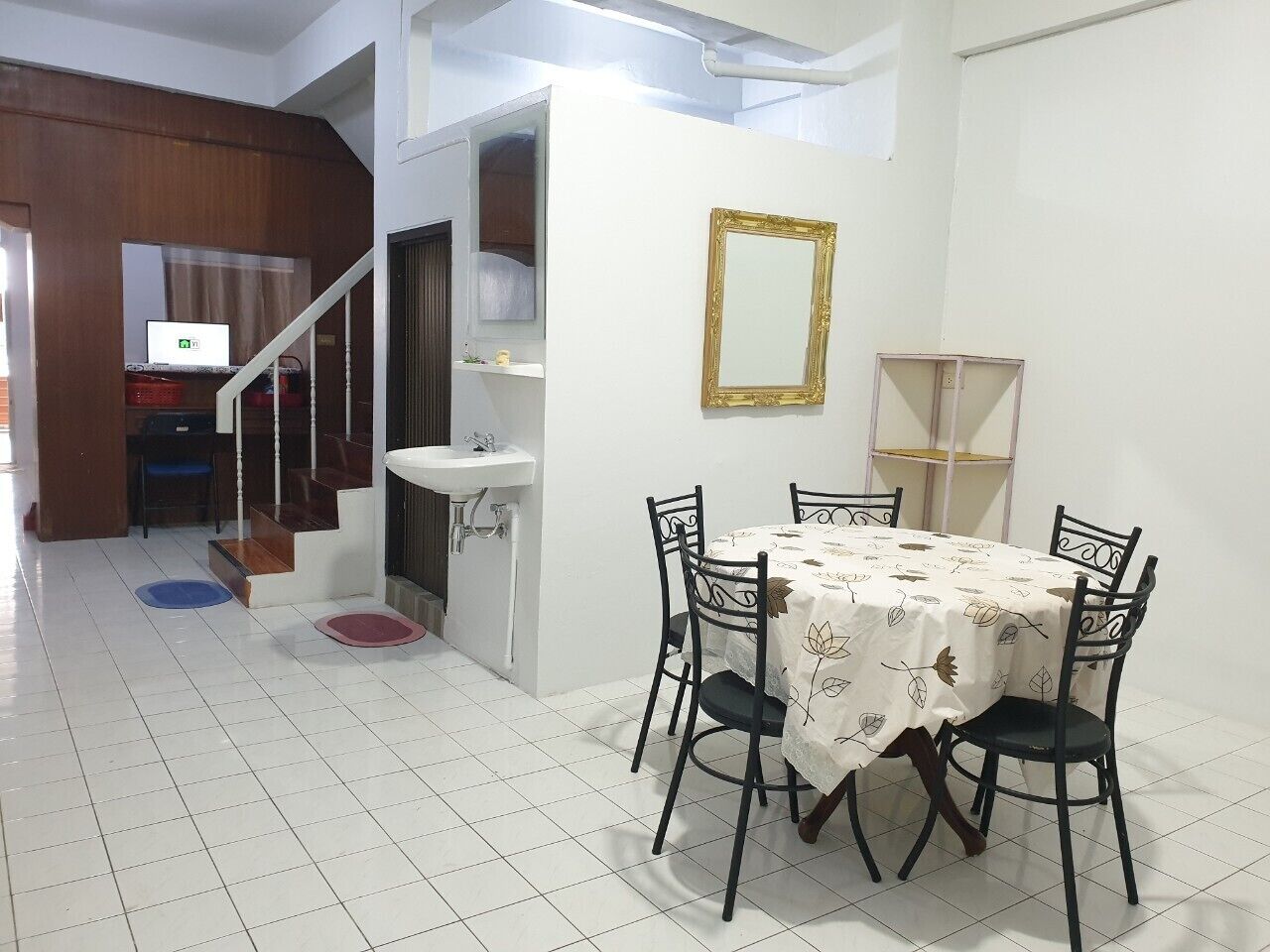 A dining area with a table and chairs, a sink, a mirror, and a staircase leading to another room.