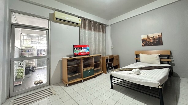 Een hotelkamer met een bed, een televisie op een houten standaard, een raam met gordijnen en een wandairconditioner.