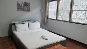 A hotel room with a bed, a headboard, a window with curtains, a wall-mounted air conditioner, and a small table with a chair.