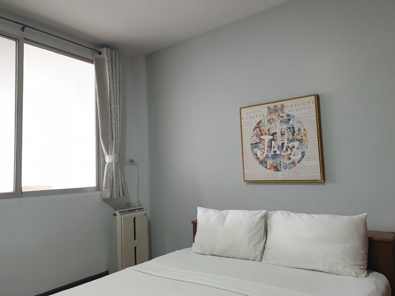 Een slaapkamer met een bed, een radiator, een raam met gordijnen en een aan de muur bevestigd fotolijstje.